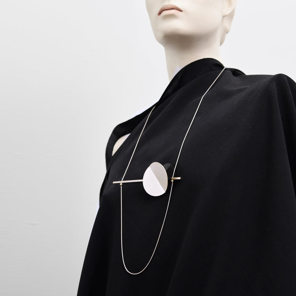 Style image of the necklace chain and geometric pendant on black fabric