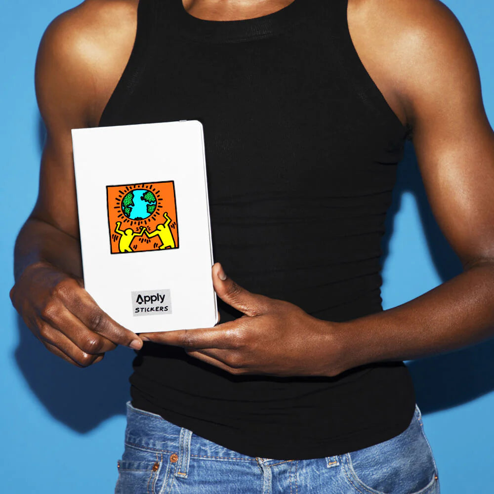 Model holding a white journal with Keith Haring Earth Sticker.