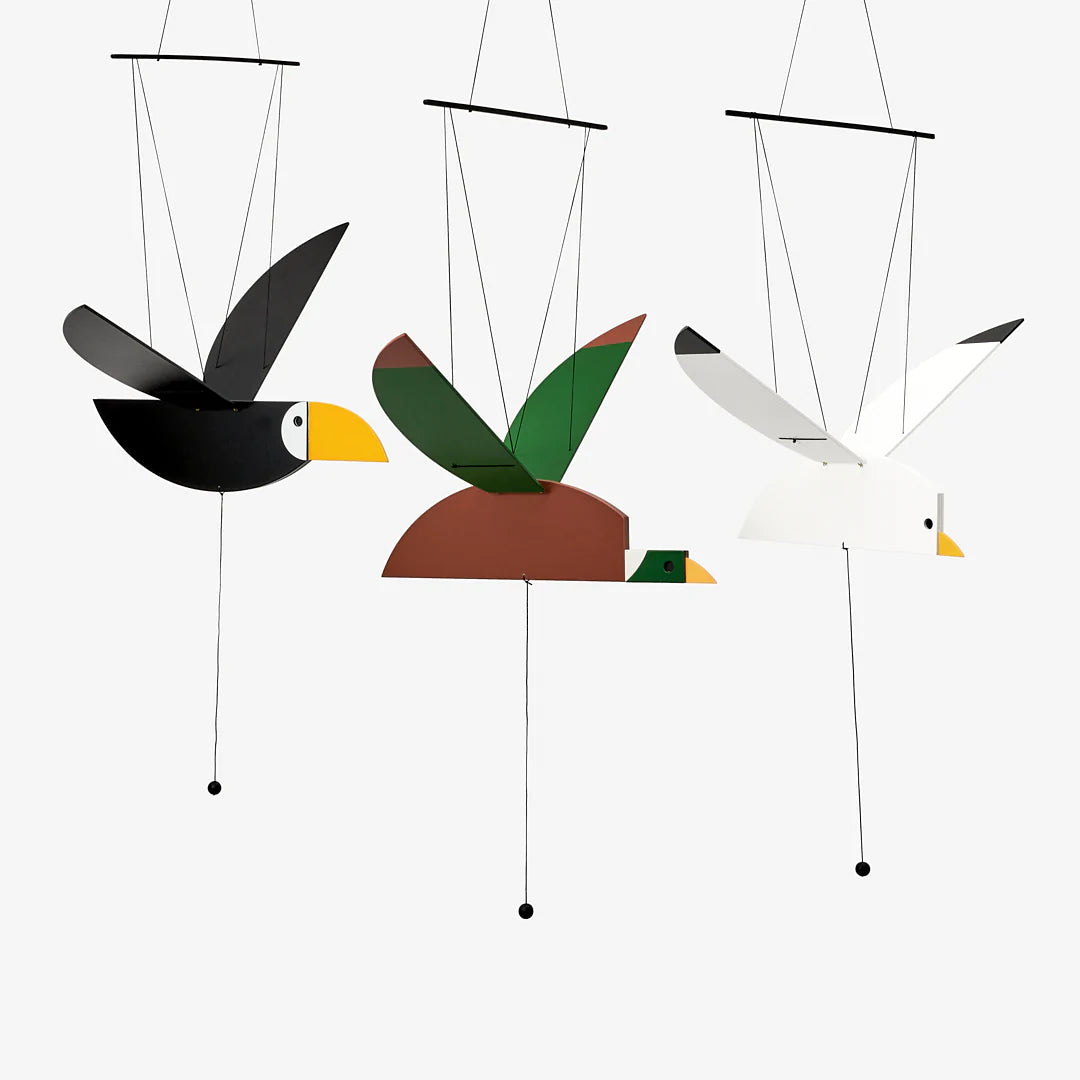 Wooden toucan mobile, painted black with a white face and yellow beak, hanging from black strings. Alongside duck and seagull mobiles.