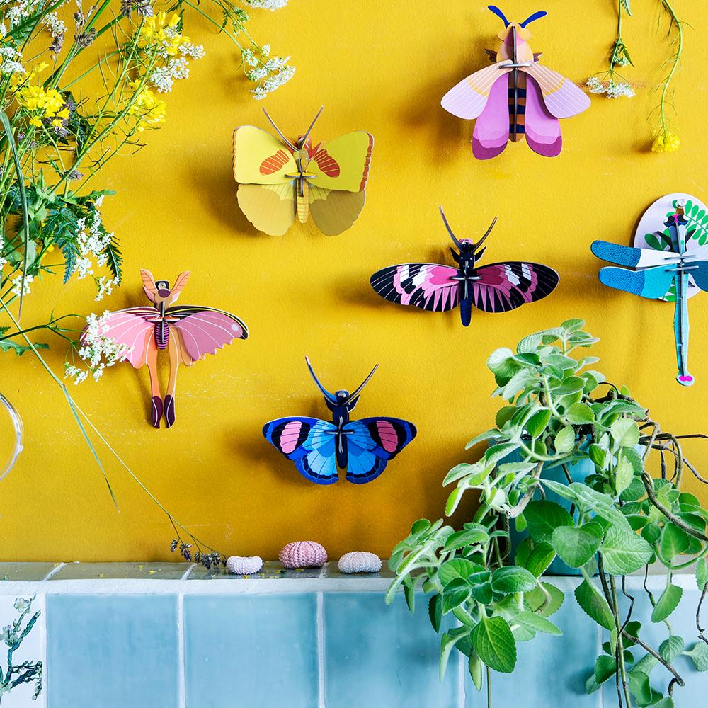 A Peacock Butterfly displayed with other paper butterflies on a wall.