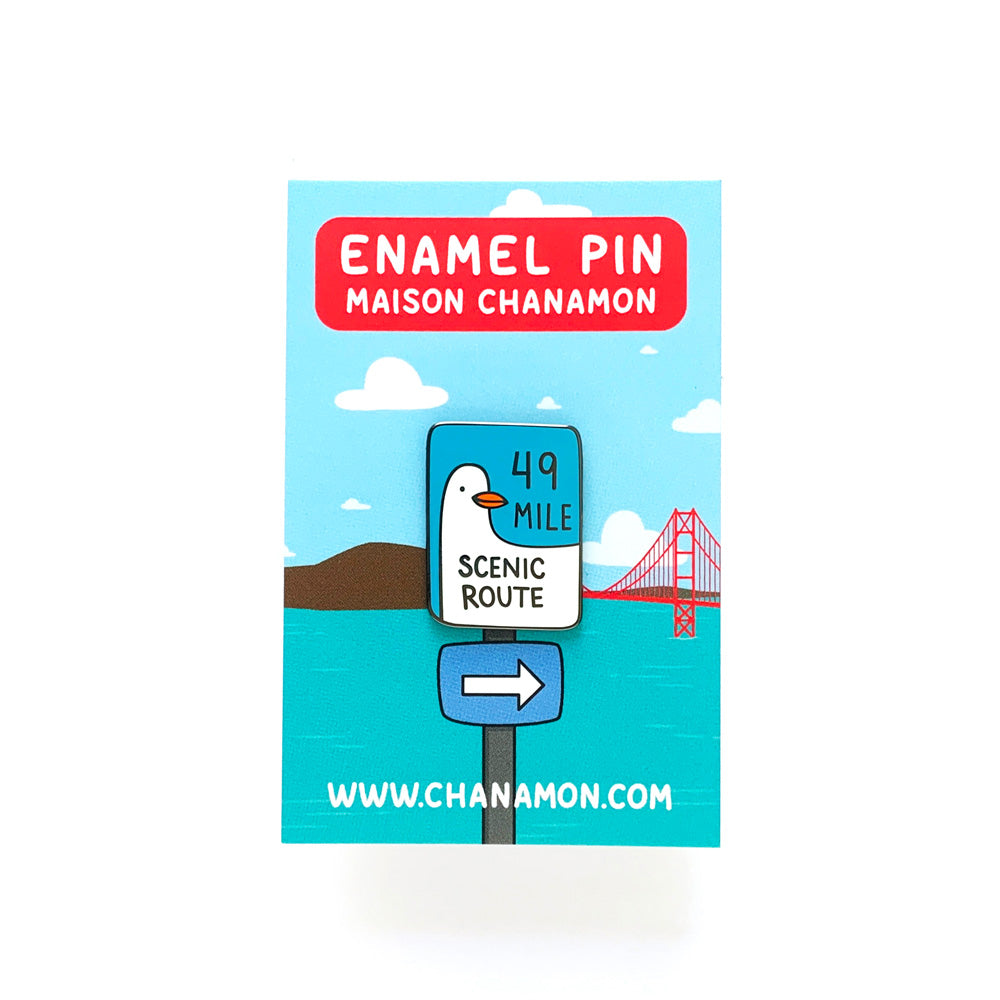 Enamel pin packaging with scenic route illustration and branding details.