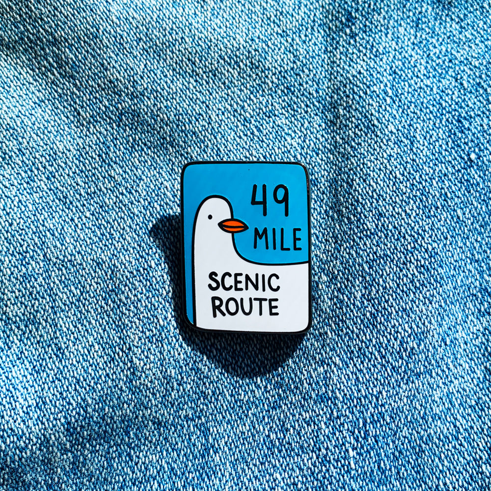 Pin with duck design and text '49 Mile Scenic Route' on a blue denim background