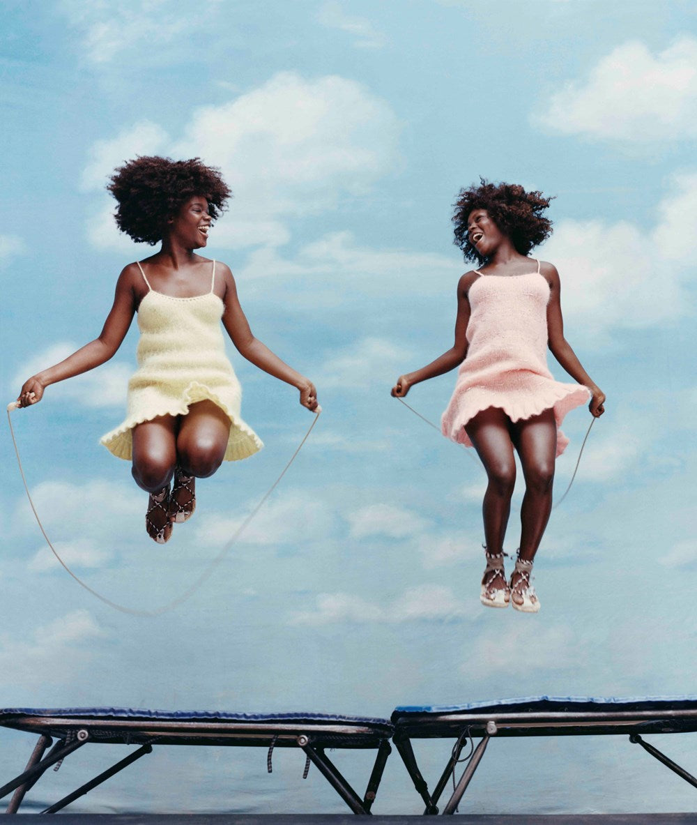 Two women jumping on a trampoline against a blue sky with clouds.