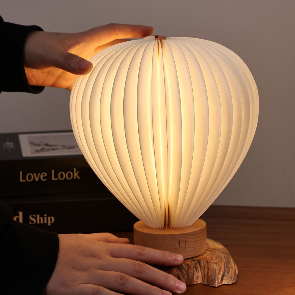 Person holding a balloon lamp with ribbed design on a wooden base, with books in the background.