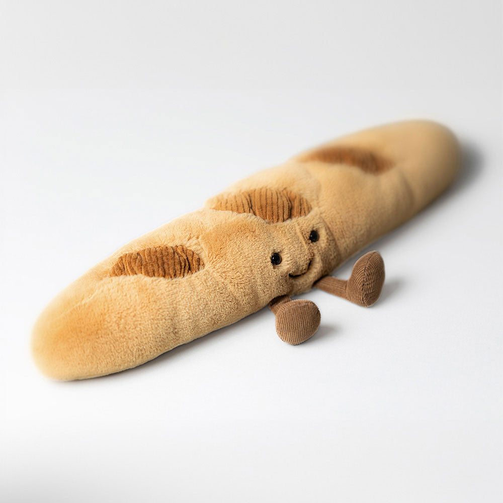Plush toy shaped like a baguette with a face on a white background