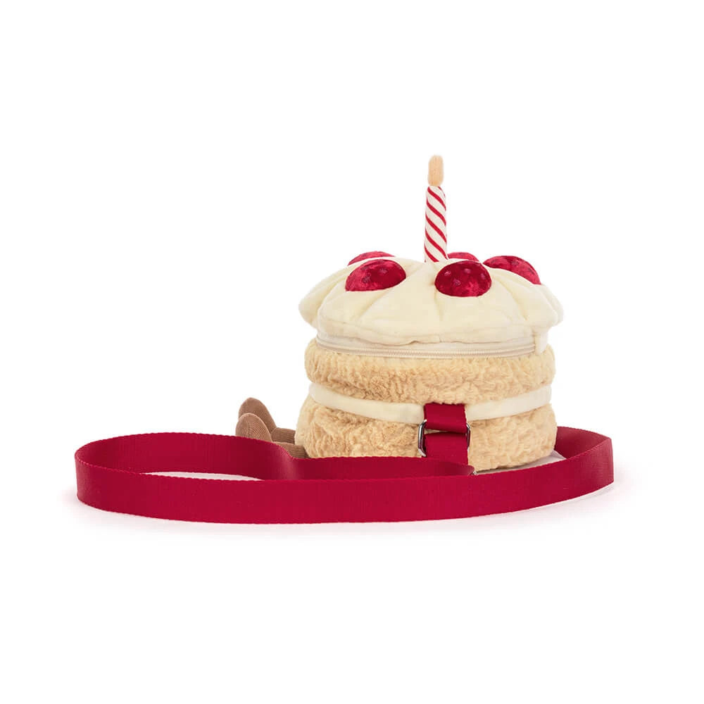 A plush cake-shaped bag with cream-colored frosting, red cherry details, a striped candle, and a red strap, shown on a plain white background.
