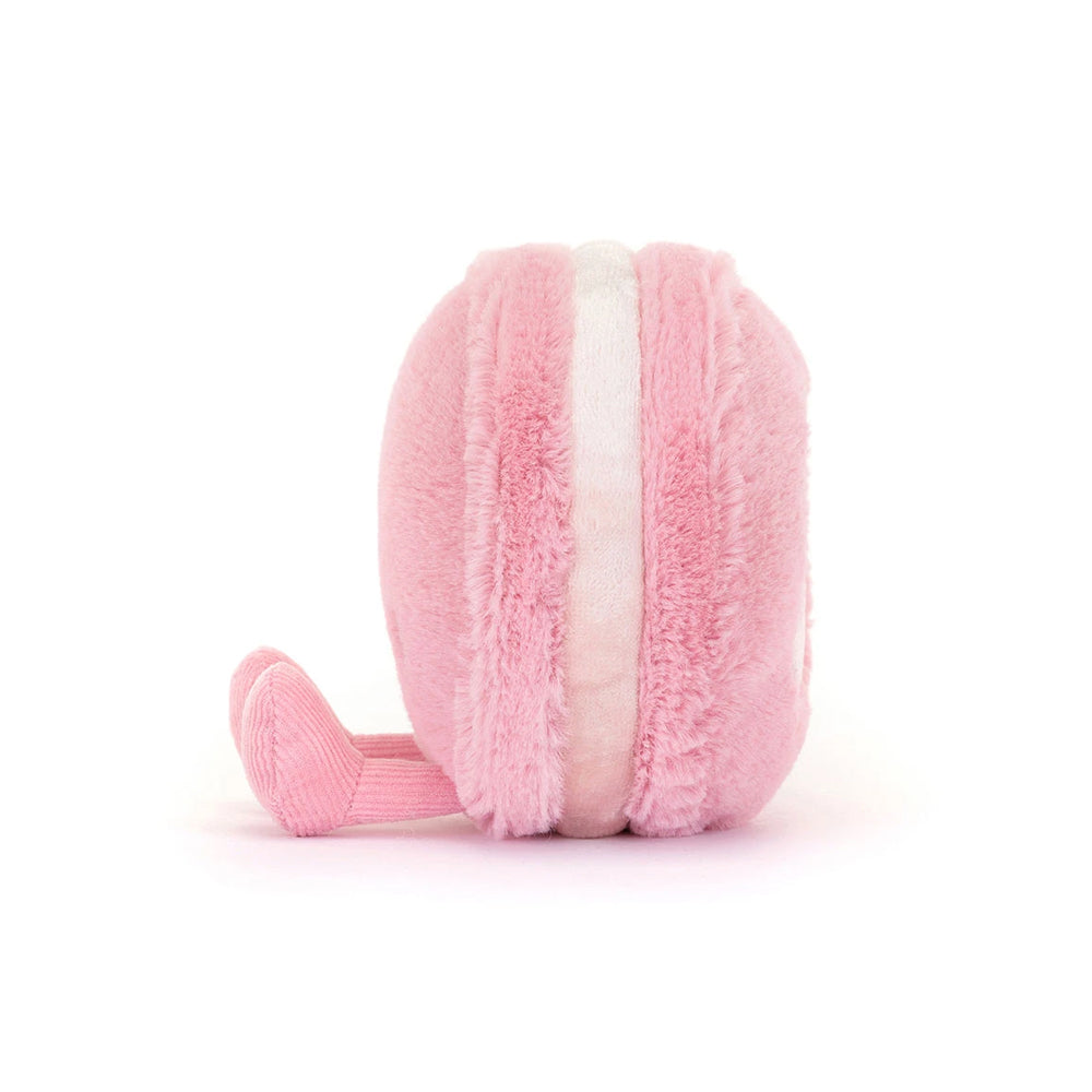 A pink plush macaron toy with a soft fuzzy texture and a small pink ribbon tail, shown from a side profile on a white background.