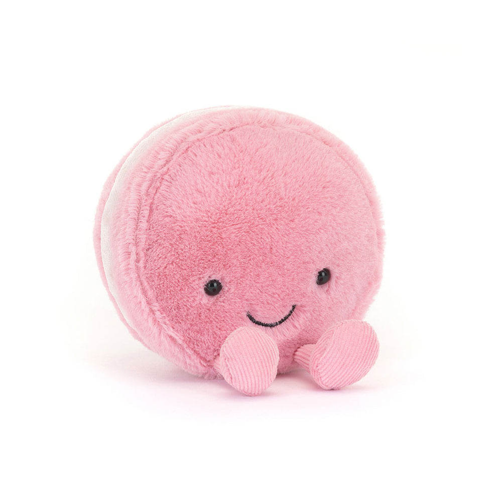 A pink plush macaron toy with a smiling face and small pink feet, photographed on a clean white background.