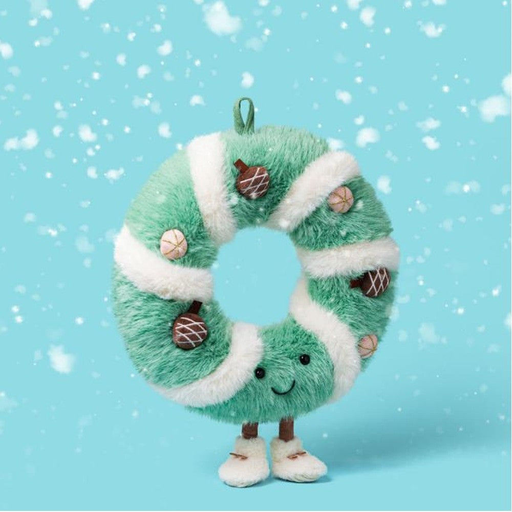 A plush Christmas wreath decoration with mint green and white stripes, small acorn ornaments, a hanging loop, and cute embroidered facial features and legs, shown against a light blue snowy background.