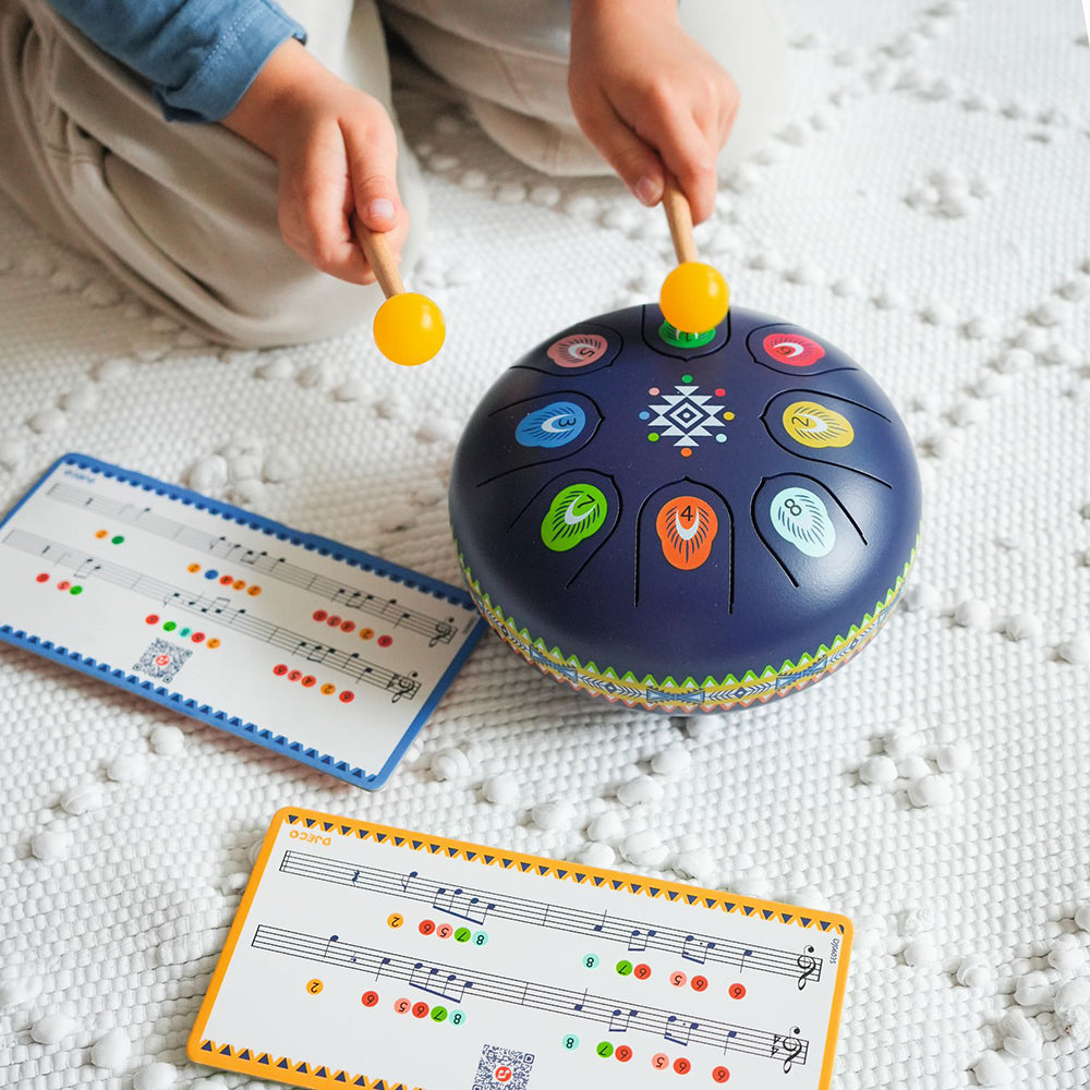 Child playing with a colorful drum toy on a textured surface with music sheets nearby.