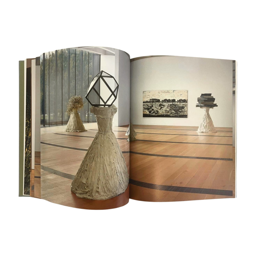 Open book showing sculptures on a wooden floor with a neutral background