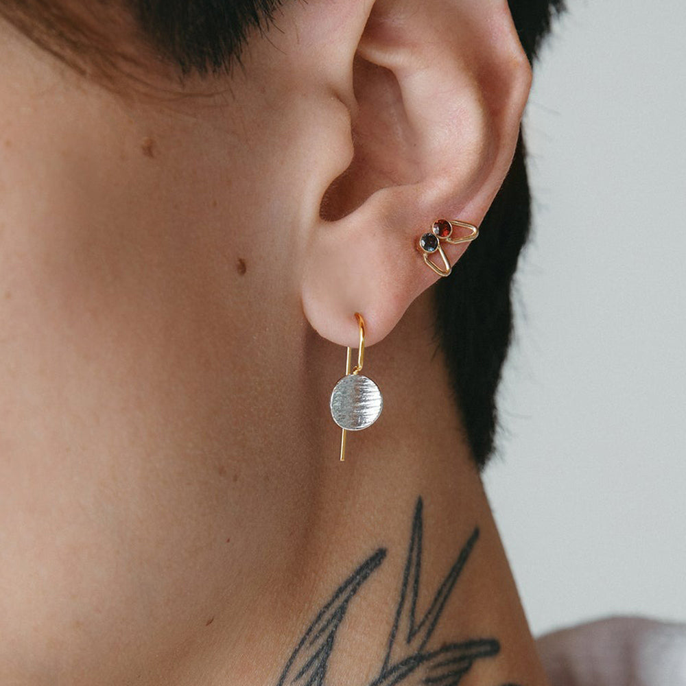 Close-up of an ear wearing gold earrings with a minimal background