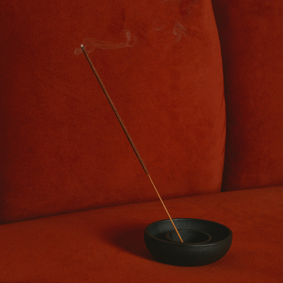 Incense stick in a black holder on a red background