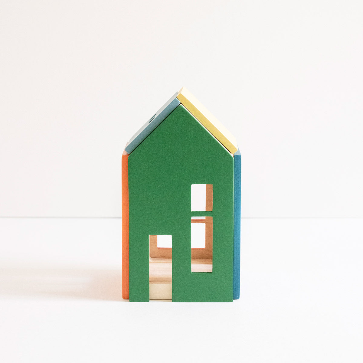 A small house-shaped wooden toy block with a green front, blue side, orange left edge, yellow roof, and natural wood interior, photographed on a clean white background.
