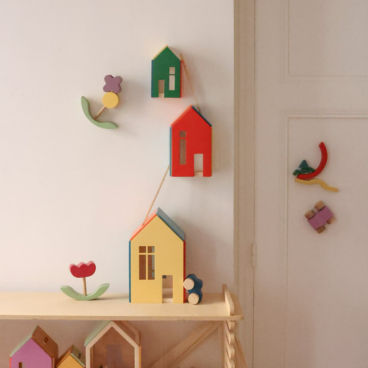 Three colorful wooden house-shaped toys in yellow, red, and green, arranged in descending size on a plain white background.