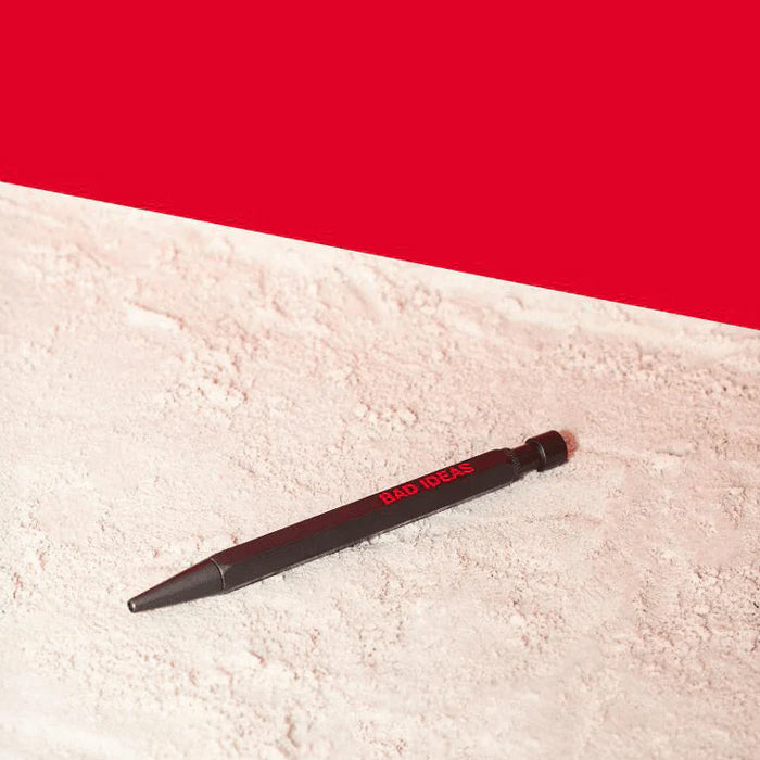 A black pen with red lettering that reads 'BAD IDEAS' lies diagonally on a textured white surface against a solid red background.