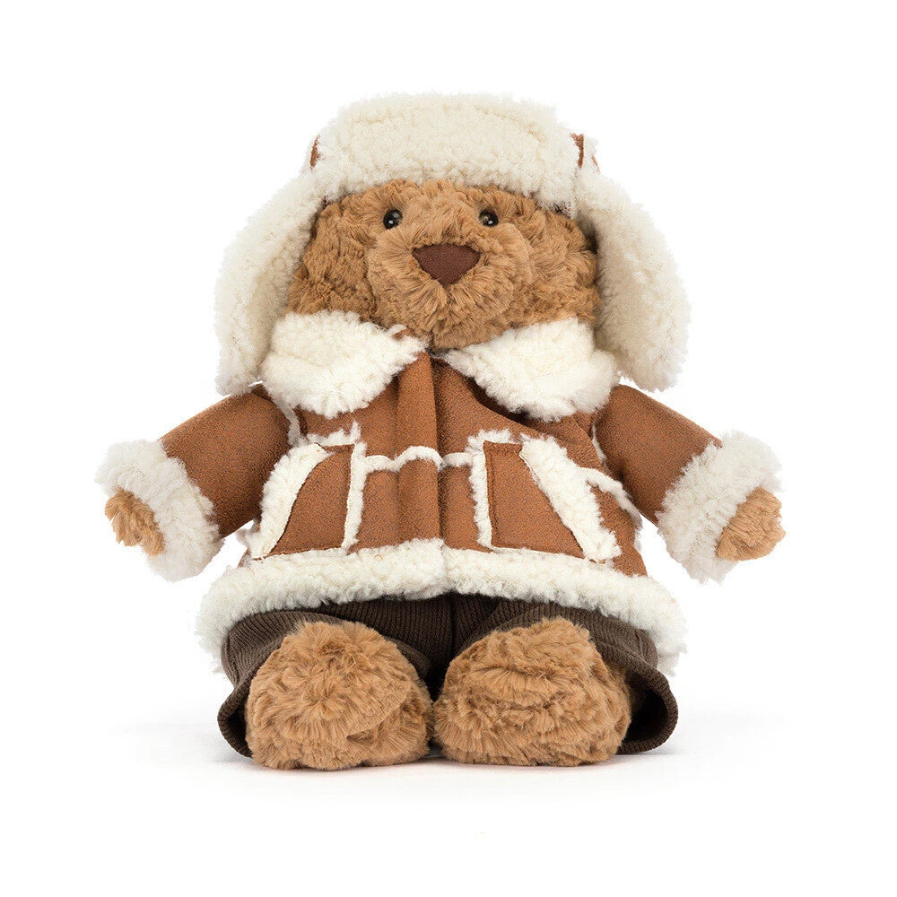 A plush teddy bear wearing a brown and cream faux-fur winter outfit with a matching hat, photographed on a clean white background.