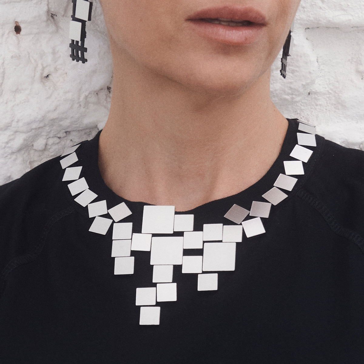 Necklace with square pendants worn by a person against a textured white background