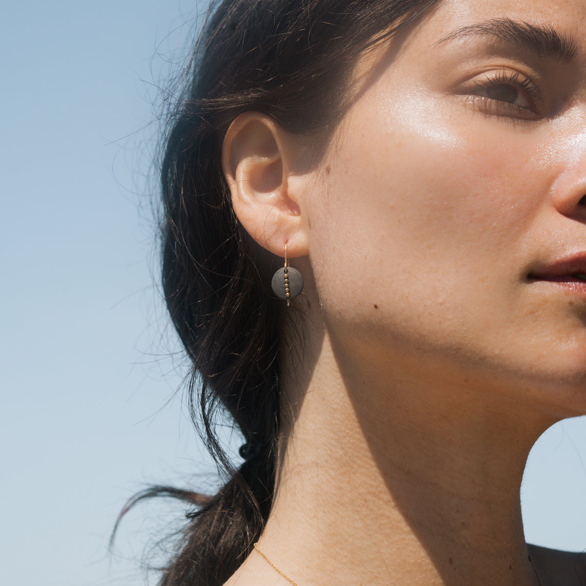 A pair of gold-tone drop earrings featuring matte black circular discs with a vertical line of small gold beads, shown on a plain white background.