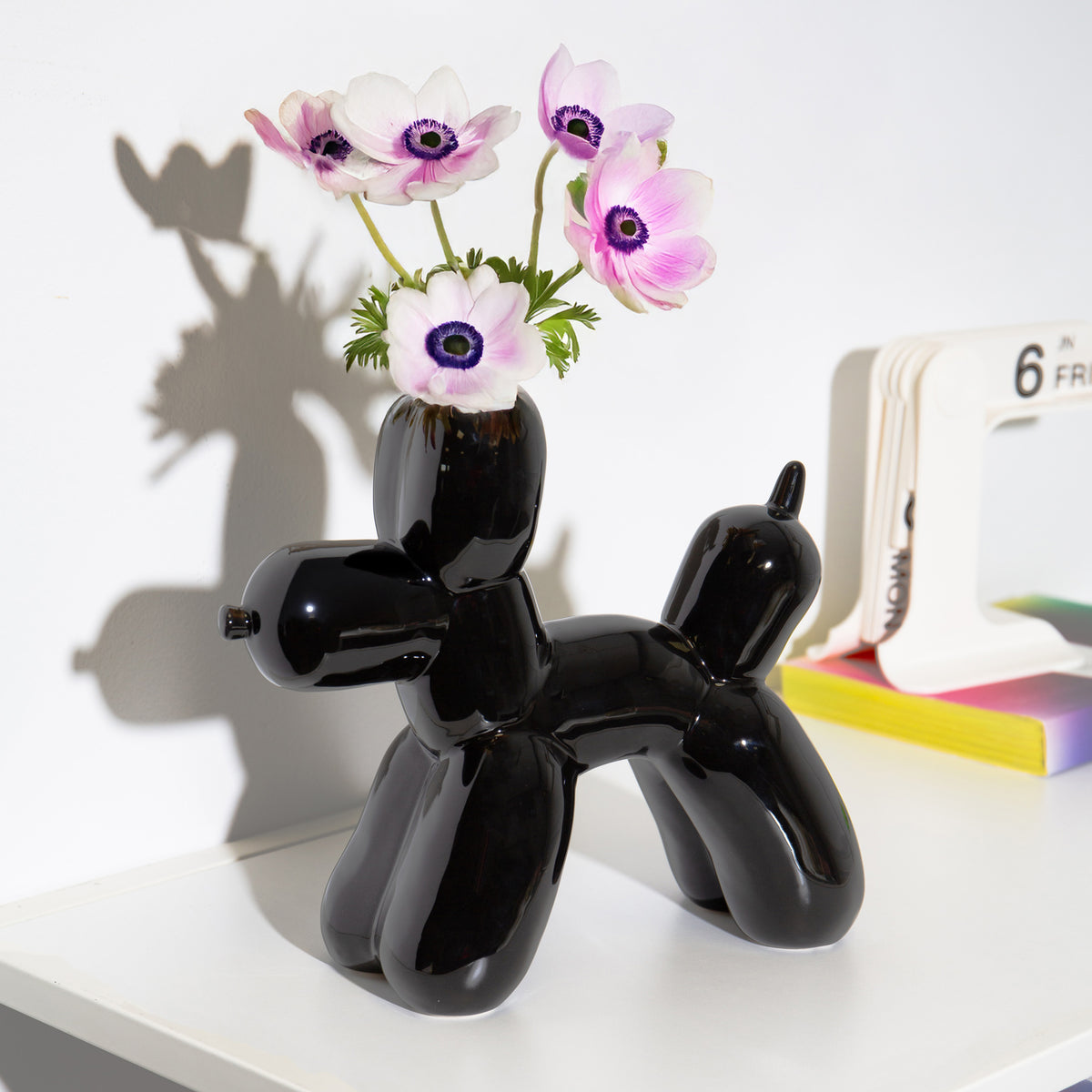 Black balloon dog-shaped vase with flowers on a white surface