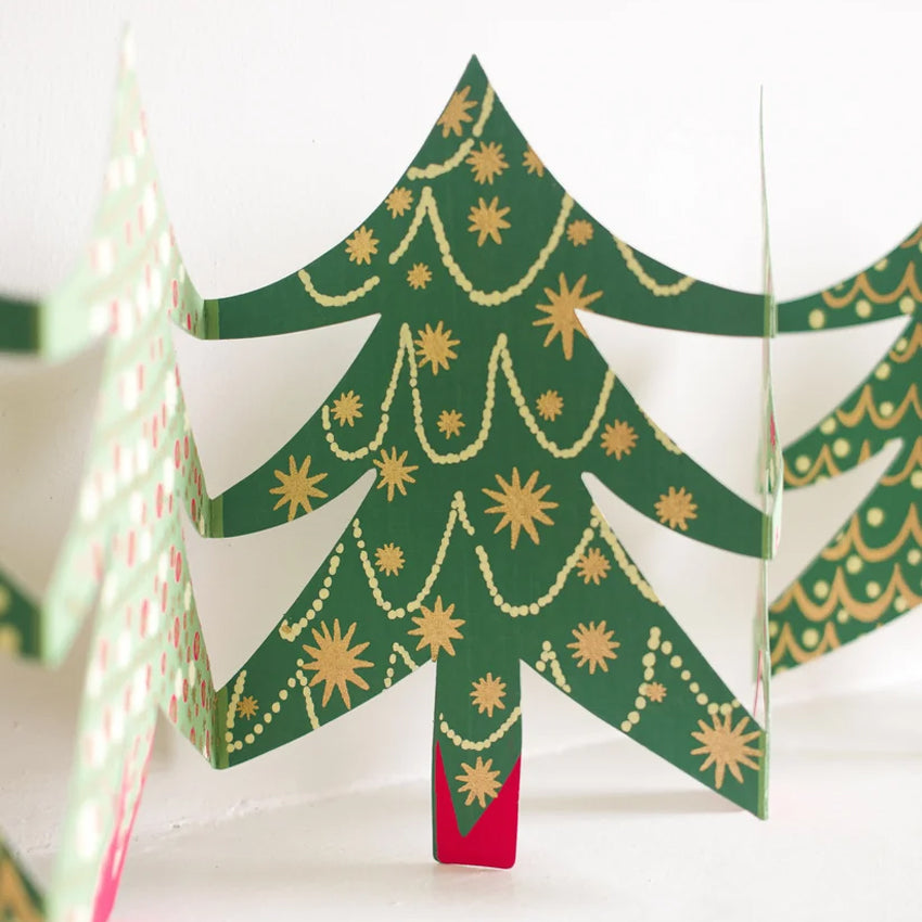 A close-up of a green Christmas tree garland with gold star ornaments and garland patterns, standing on a white surface with other partially visible tree cards in the background.