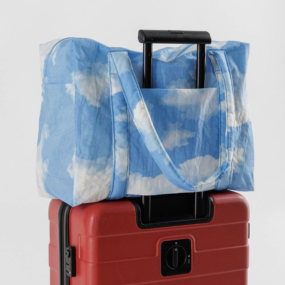 Cloud Carry-on tote in Clouds print, resting on top of red luggage.