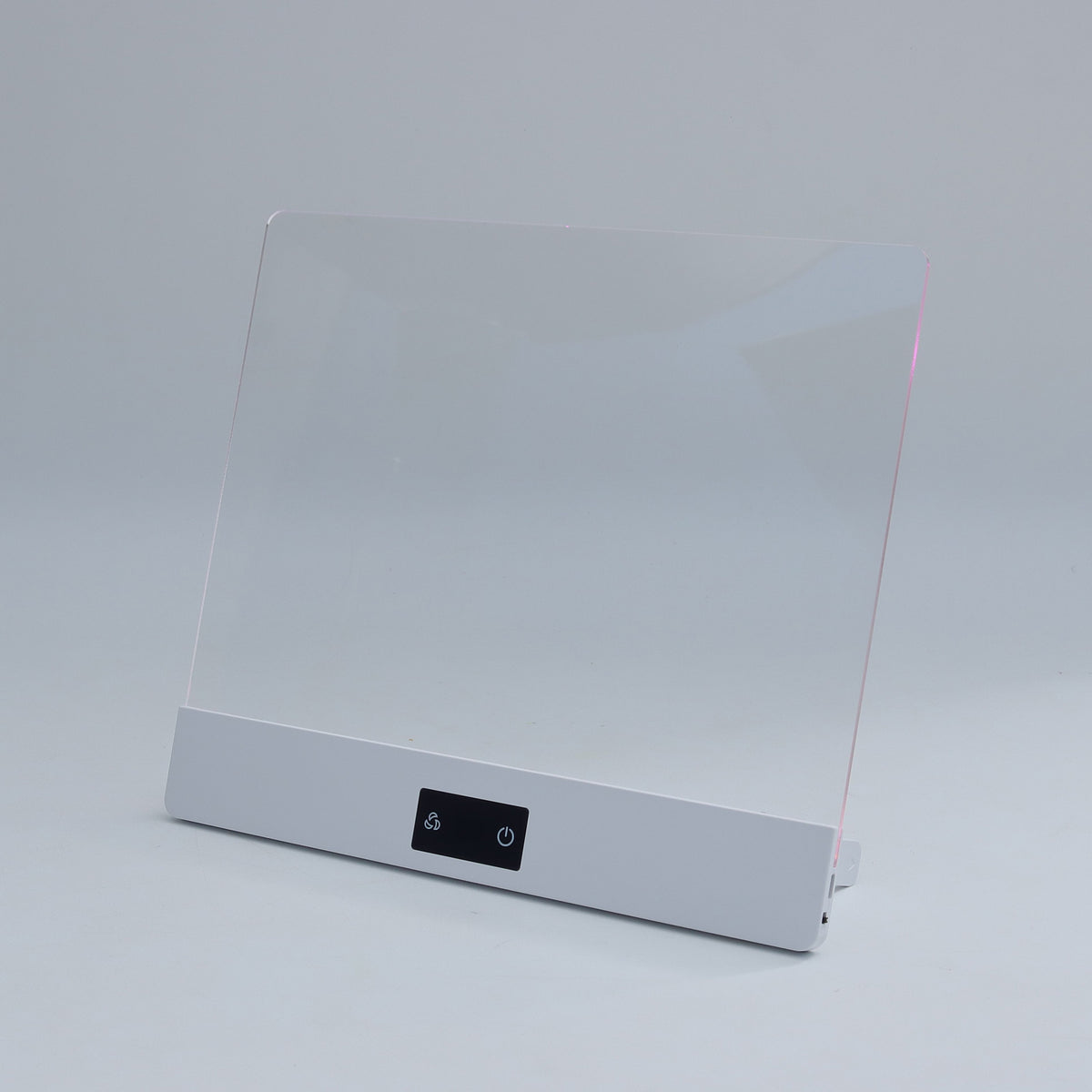A modern white electronic device with a large clear acrylic panel on top and a small black control button panel on the front, set against a neutral light gray background.