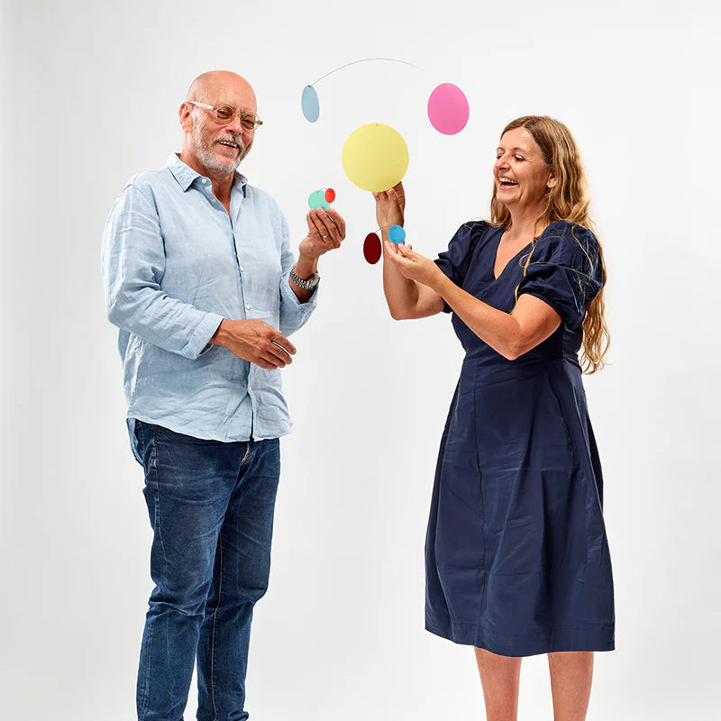 Man and woman playing with colorful hanging mobiles against a white background