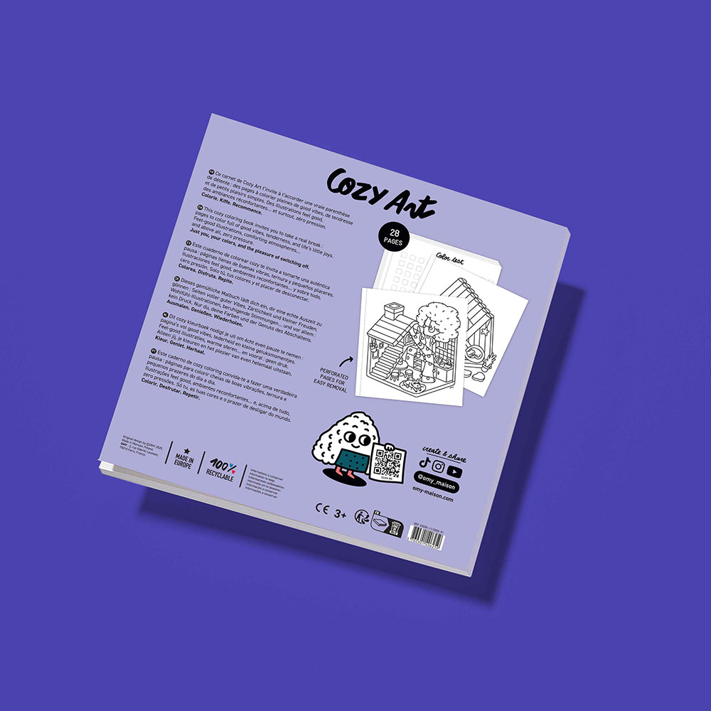 The back cover of the 'Cozy Art' book, angled on a solid purple background. The cover is a pale lavender color with black text, illustrations of a cozy room, and small product photos showing the contents inside.