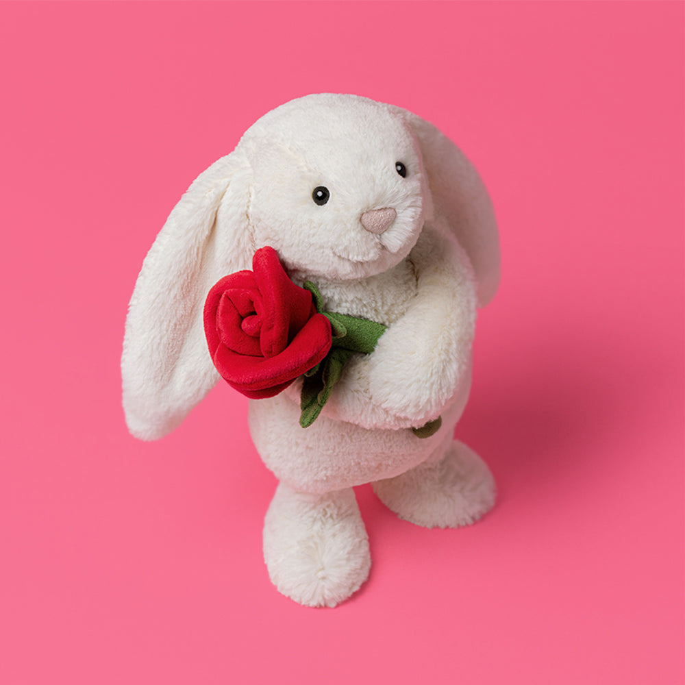 White plush bunny holding a red rose on a pink background