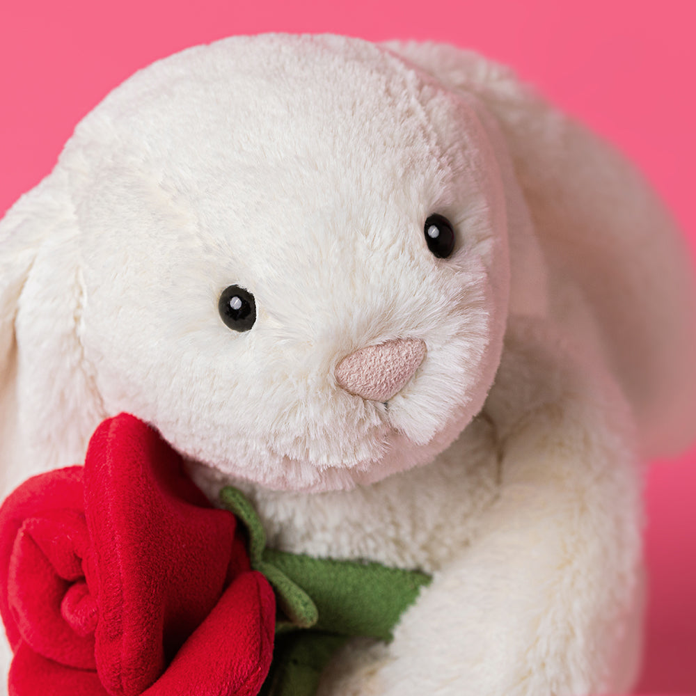 White plush bunny holding a red rose against a pink background