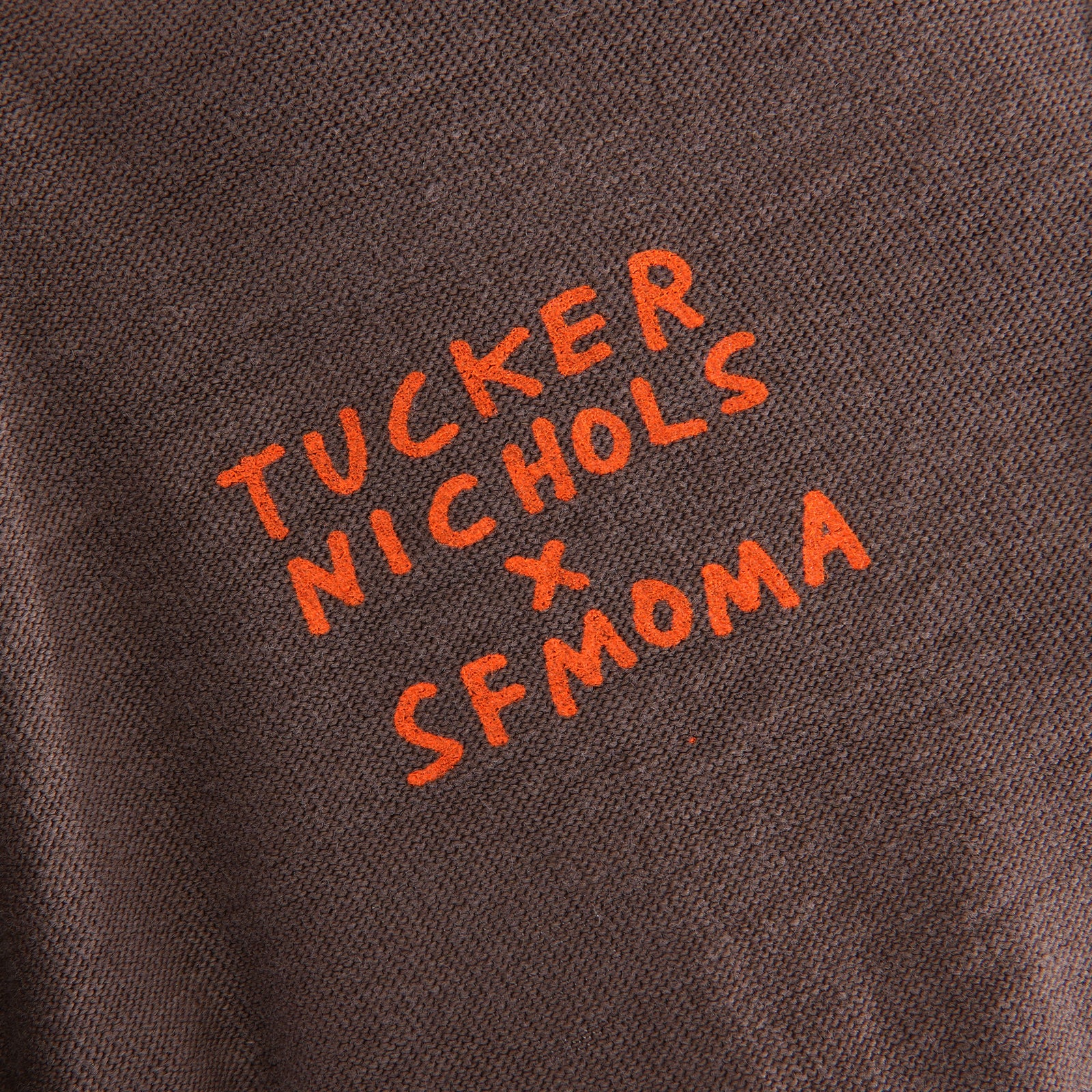 A dark gray short-sleeve crewneck t-shirt featuring the word 'SFMOMA' printed in a bright blue stylized stacked graphic on the chest, displayed flat against a white background.