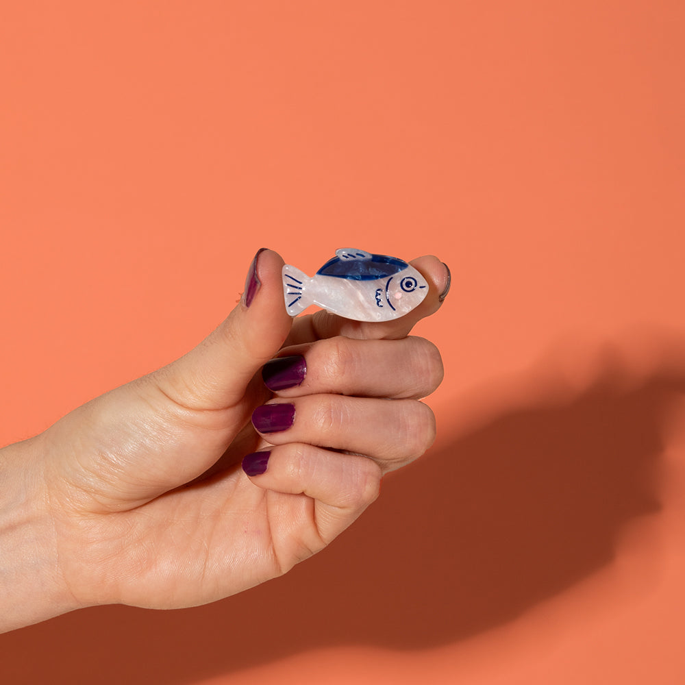 Hand holding a small fish-shaped clawvagainst an orange background
