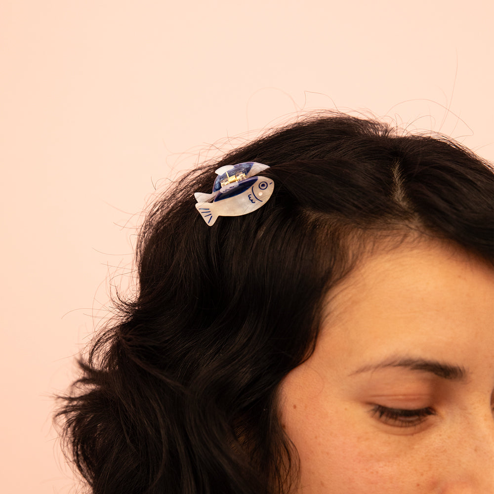 Person wearing a decorative fish-shaped hair claw on a pink background