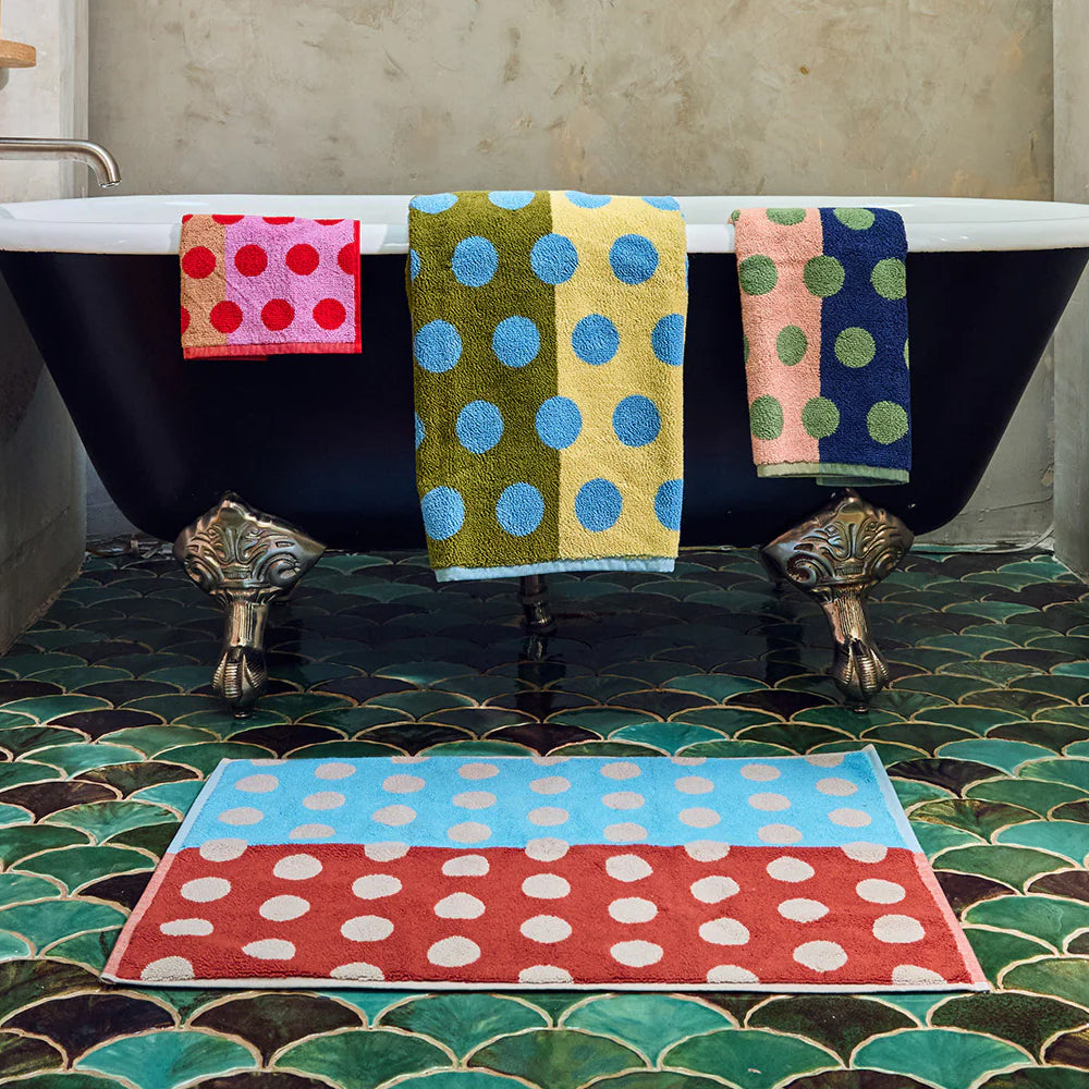 Colorful polka dot towels hanging over a bathtub with a matching rug on the floor.