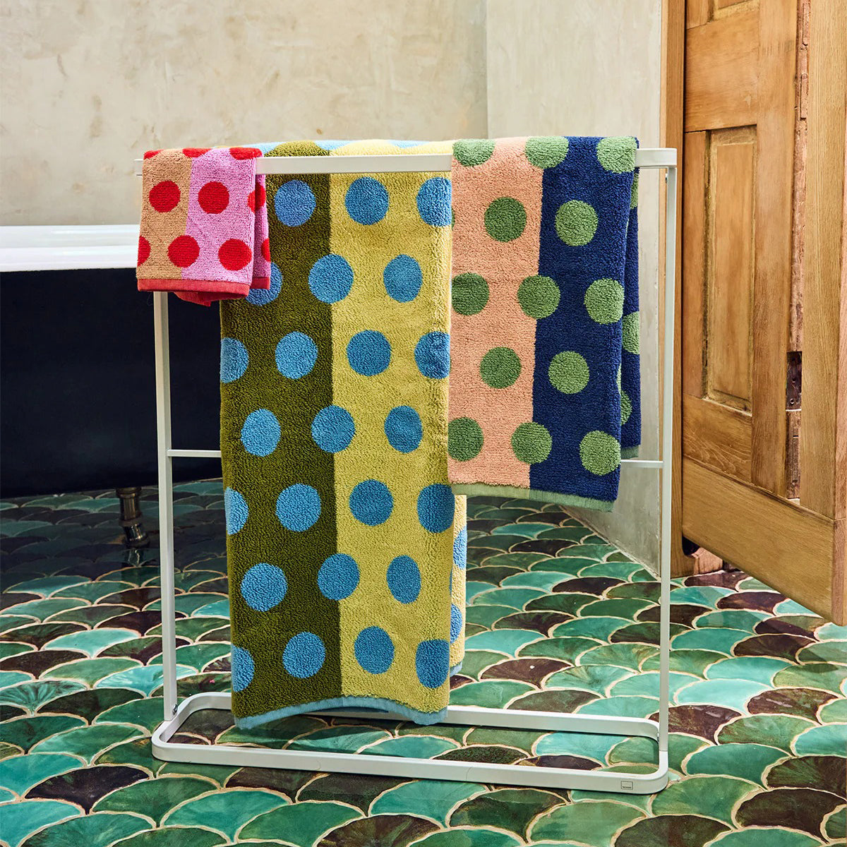 Colorful polka dot towels on a metal towel rack with a tiled bathroom floor.