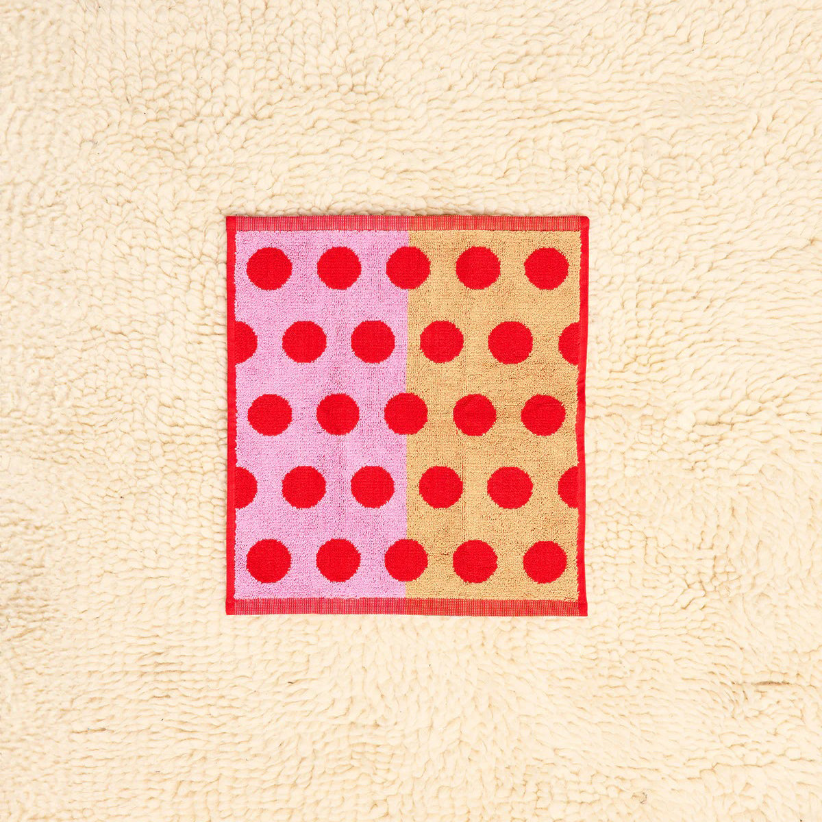 Rectangular towel with pink and beige sections and red polka dots on a textured beige background