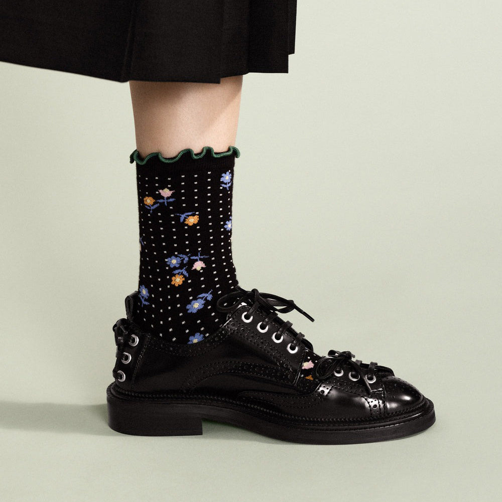 Black lace-up boots with floral-patterned socks on a neutral background