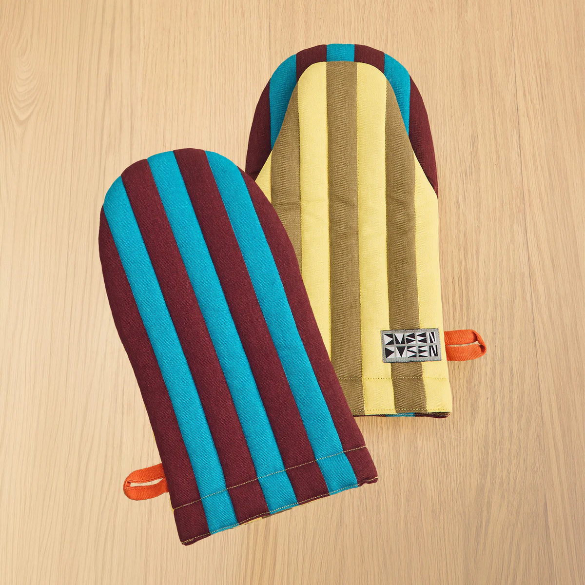 Colorful striped oven mitts on a wooden surface with a visible brand logo.