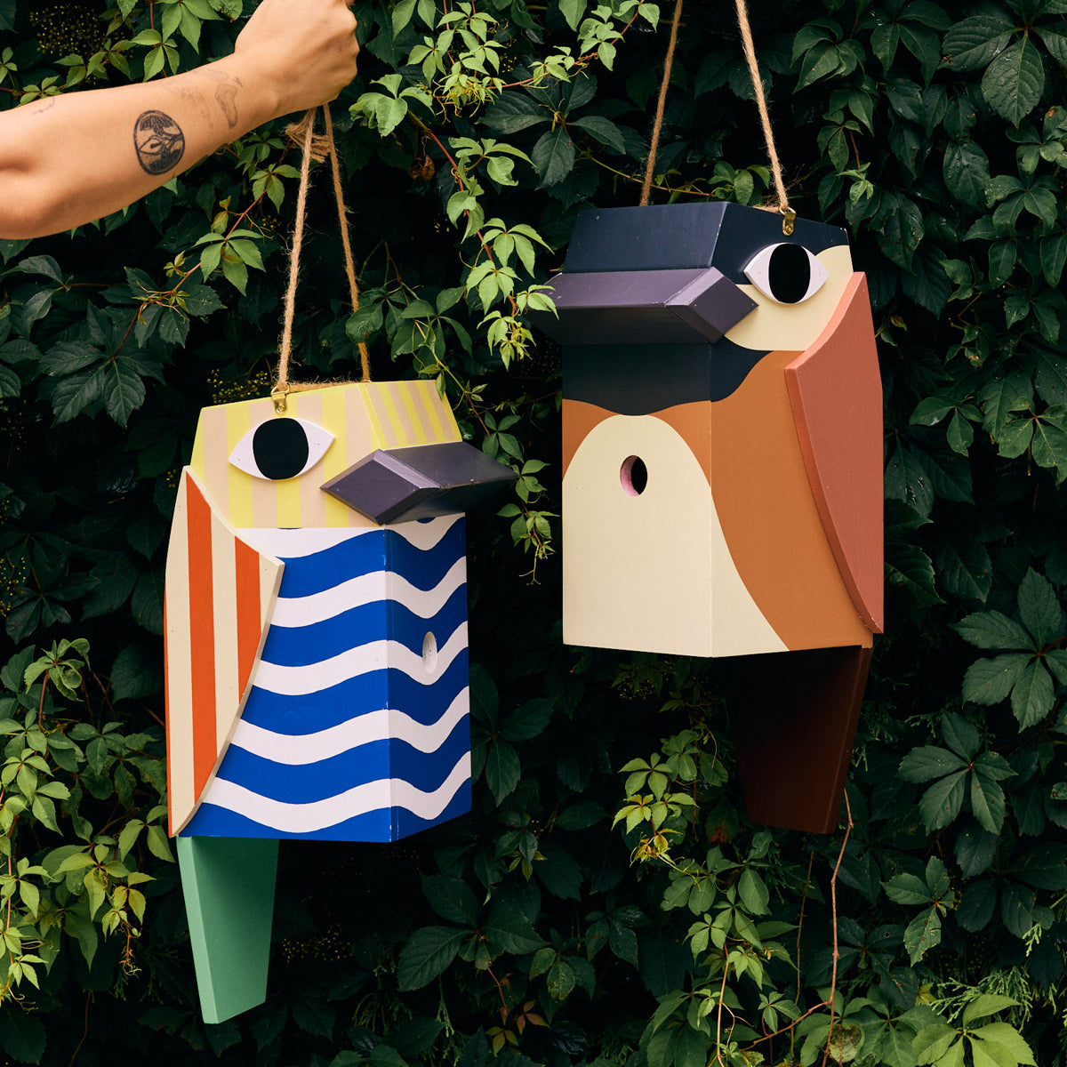 Two colorful birdhouse designs hanging against a green leafy background