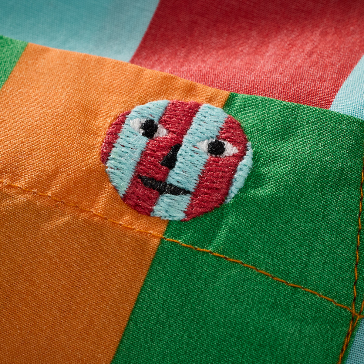 Close-up of a colorful patchwork with embroidered faces on the fabric, featuring orange, green, red, and light blue sections.