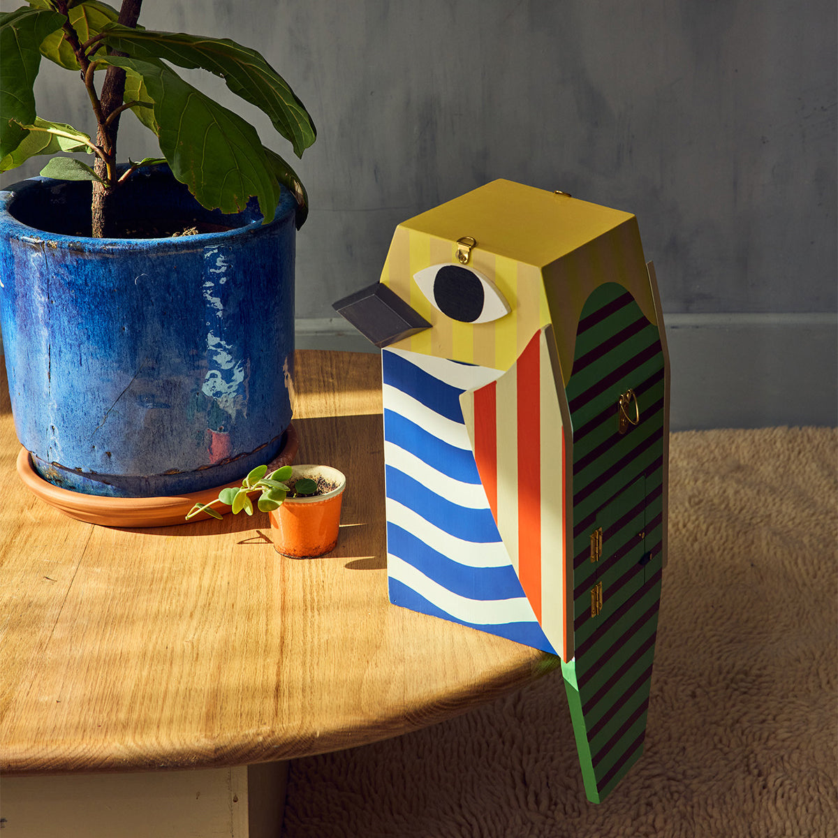 Colorful bird-shaped birdhouse on a wooden surface with plants in the background