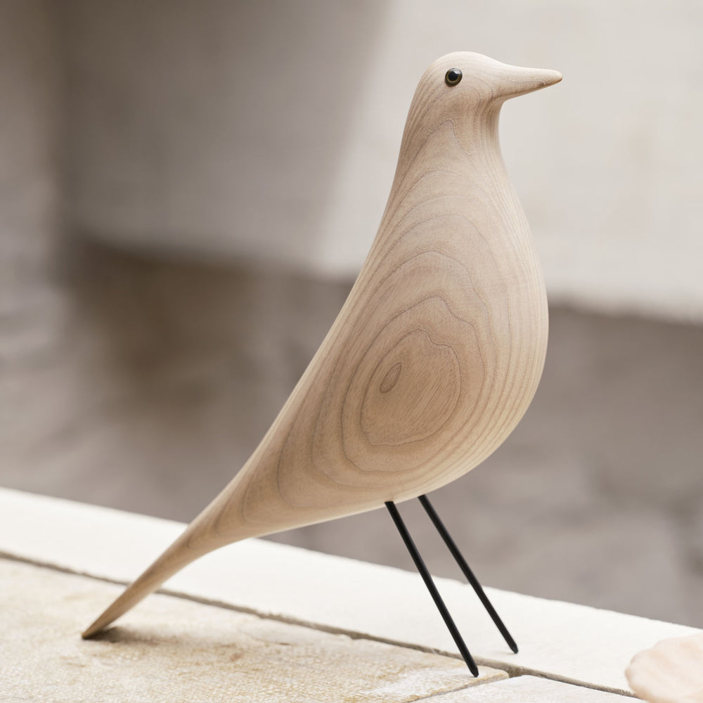 Wooden bird sculpture with black legs on a neutral background