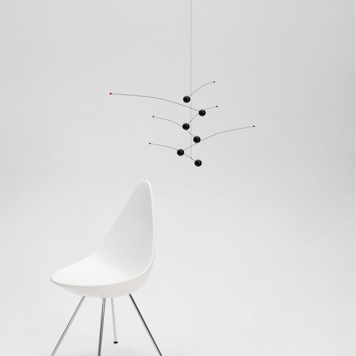 Modern white chair with a minimalistic black and red hanging sculpture on a light gray background