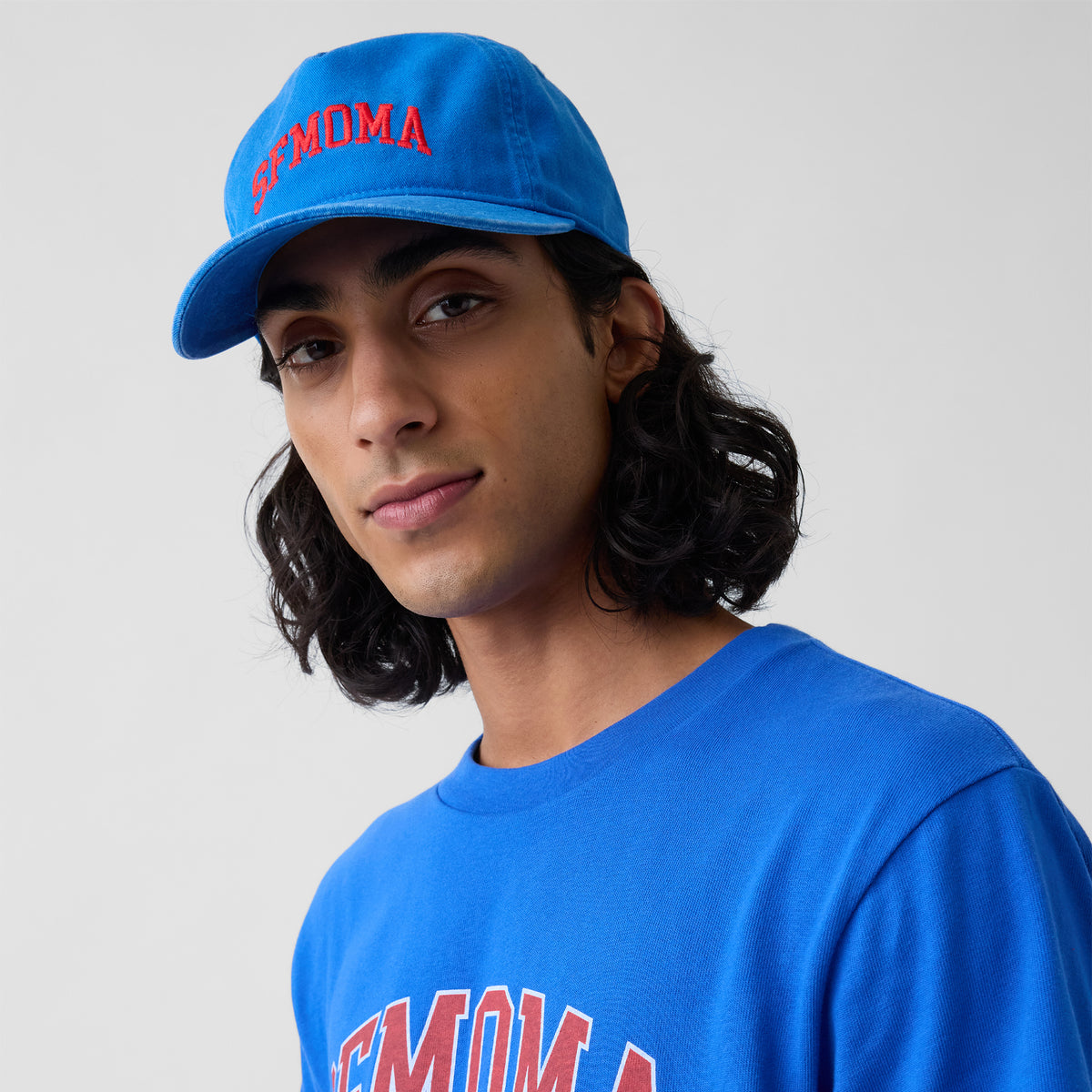 A blue baseball cap with 'SFMOMA' embroidered in red arched lettering on the front, shown on a clean white background.