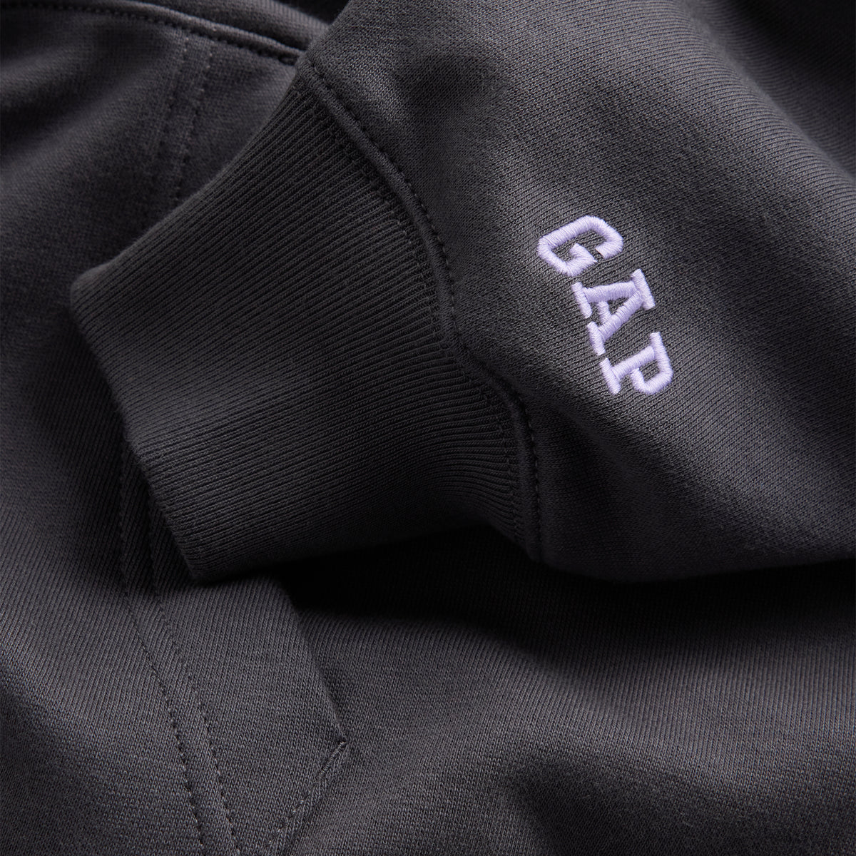 Close-up of a dark charcoal gray ribbed fabric garment with a white embroidered 'GAP' logo on the sleeve.
