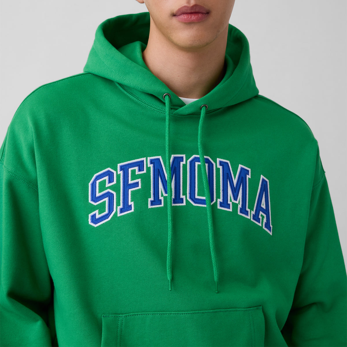 A bright green pullover hoodie with 'SFMOMA' printed in blue varsity-style lettering across the chest, shown against a plain white background.