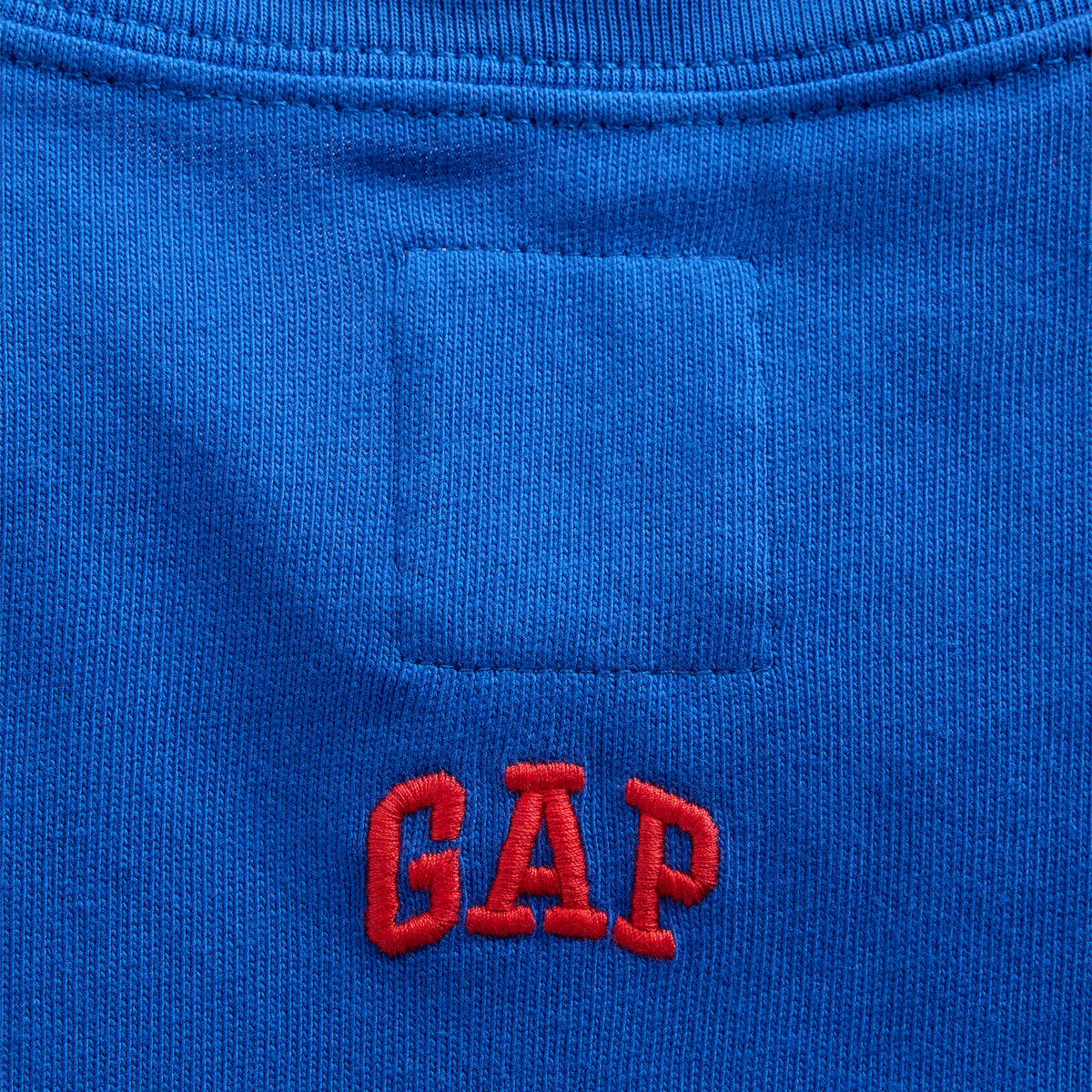 Close-up of a bright blue knit garment showing a red embroidered GAP logo below a rectangular patch pocket.