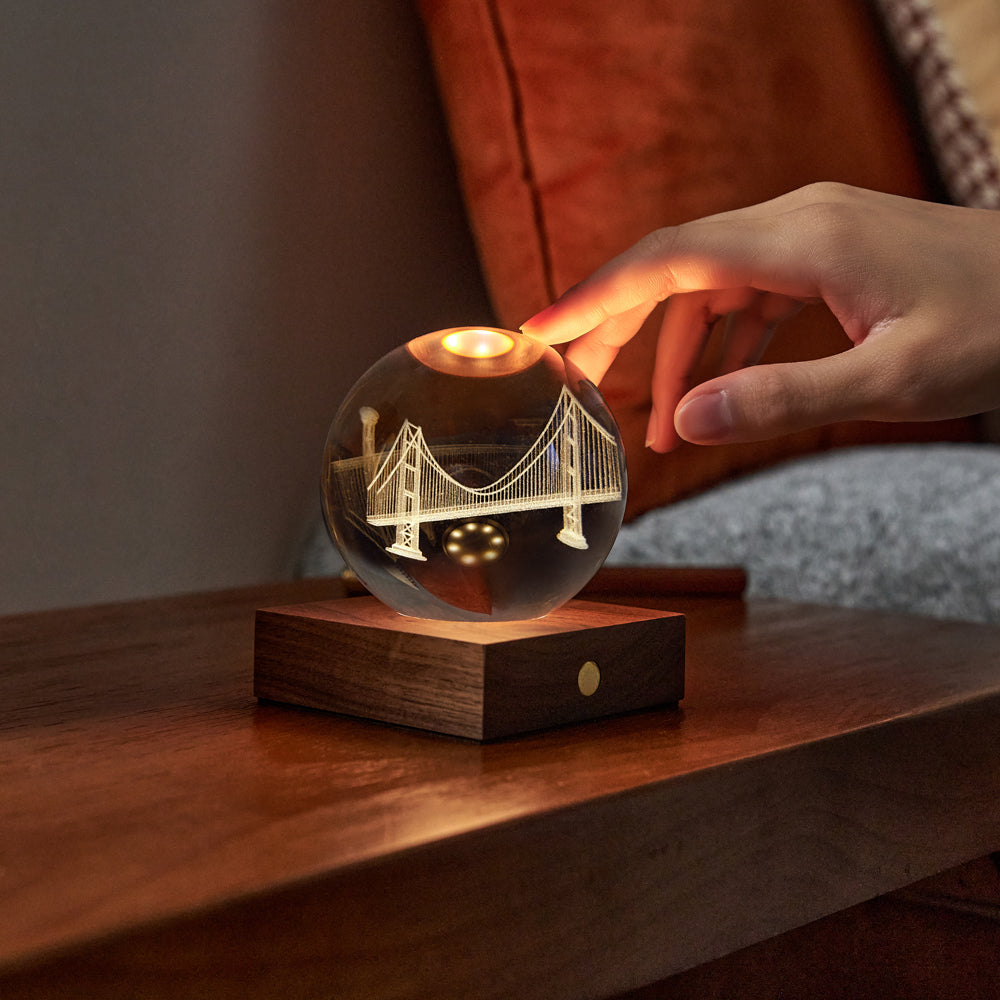Glass ball with bridge design on a wooden base, held by a hand.