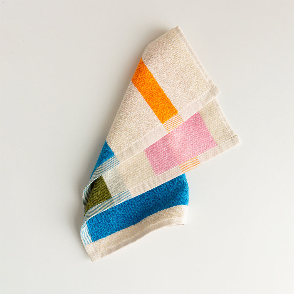 An open white gift box containing six rolled bath hand towels in assorted pastel and bright colors, with a printed beach scene on the inside lid. 